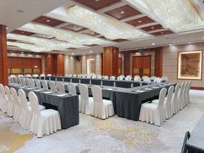 Un salón de conferencias con una larga mesa, sillas blancas y una araña.