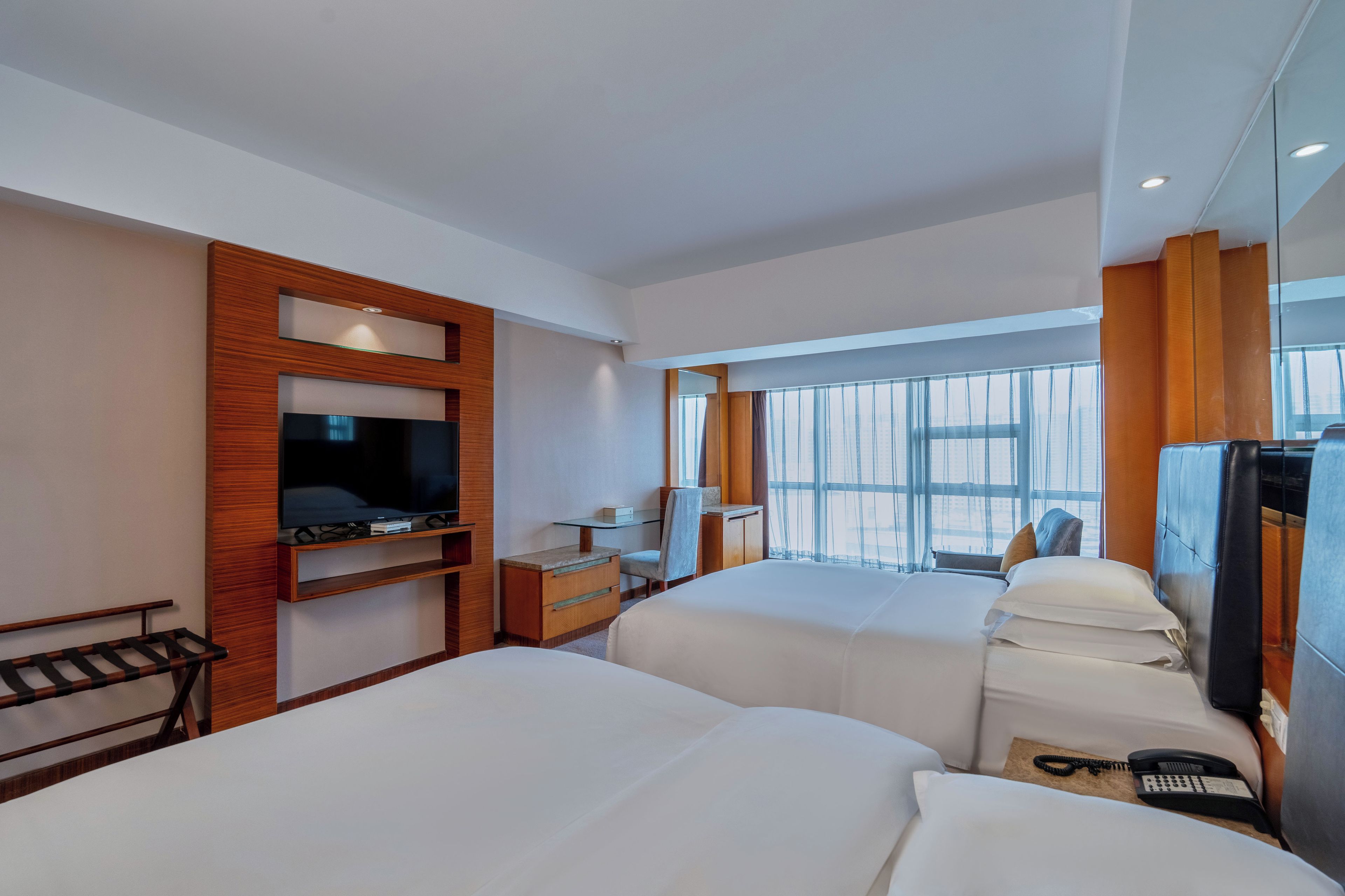 A hotel room with two beds, a TV, a desk, and a window with a view.