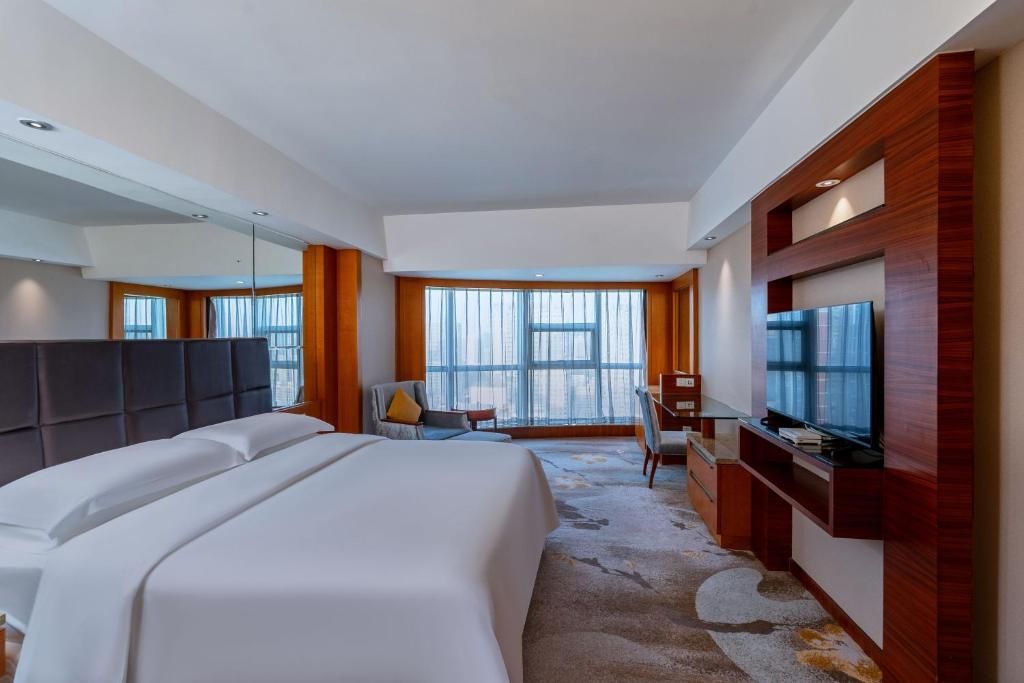 A hotel room with a large bed, a TV, a desk, and a chair.