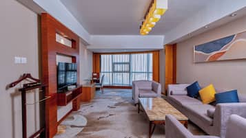 Habitación de hotel moderna con sofá, sillón, televisor y vista a la ciudad.