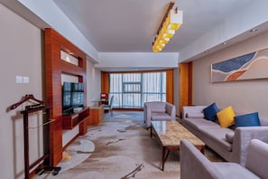 Habitación de hotel moderna con sofá, sillón, televisor y vista a la ciudad.