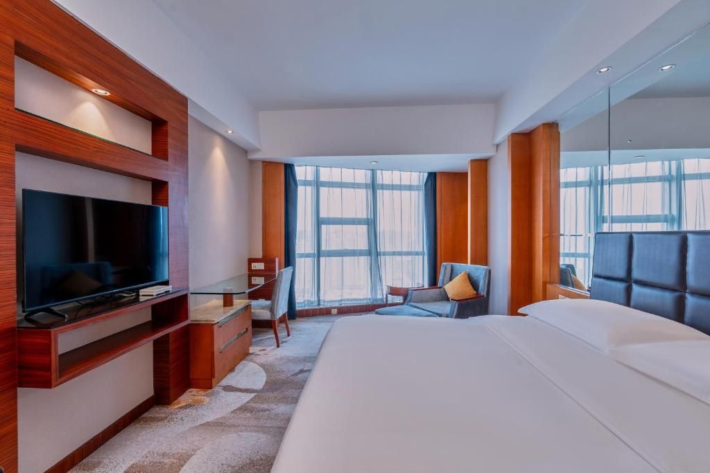 A modern hotel room with a large bed, a flat-screen TV, a desk, and a chair.