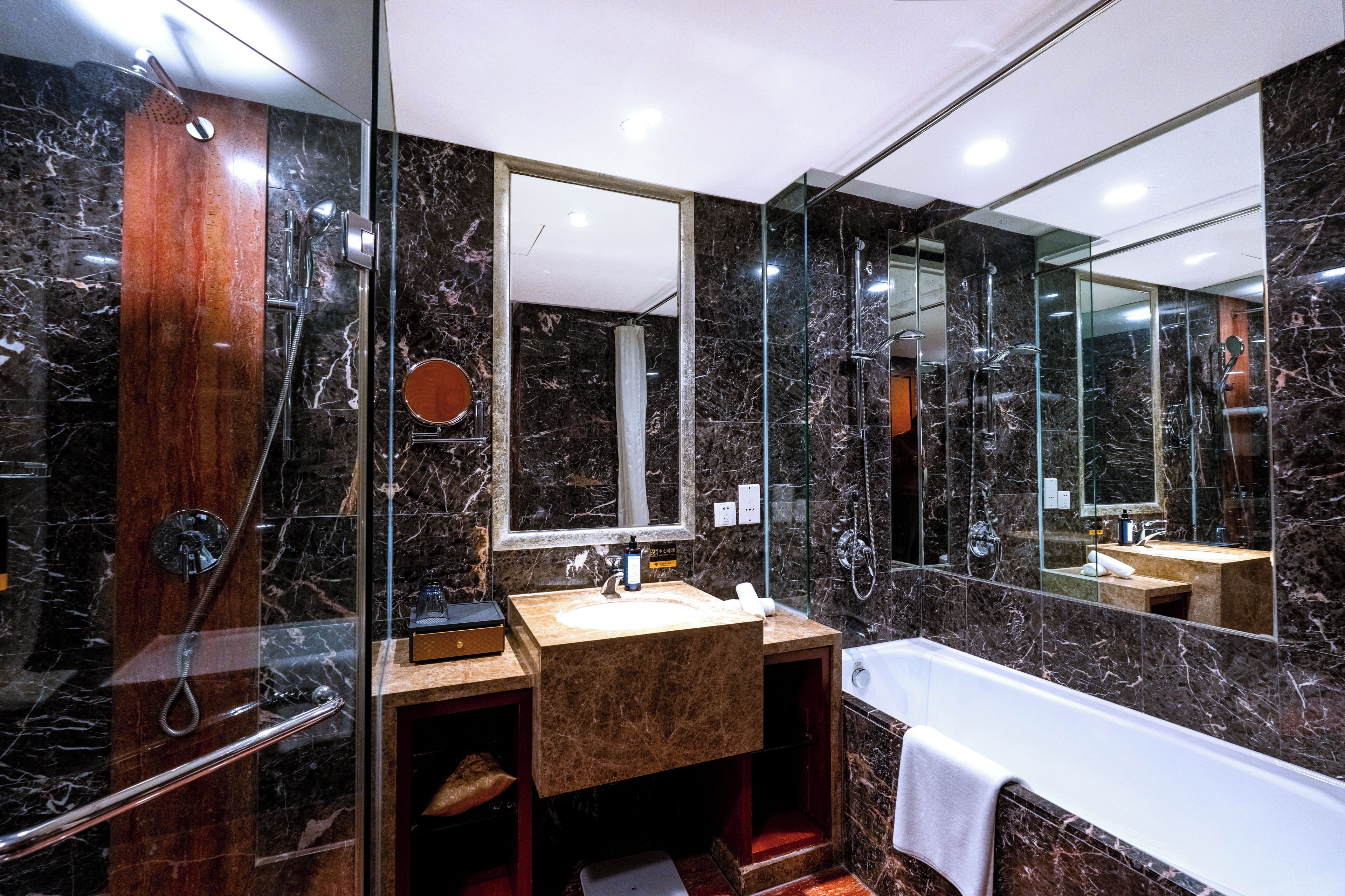 A modern bathroom with a marble shower, a wooden vanity, and a large mirror.