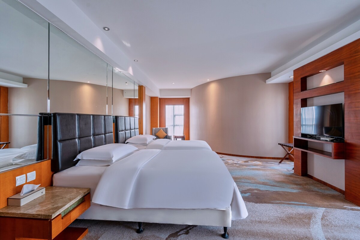 A hotel room with a large bed, a TV, a desk, and a mirror.