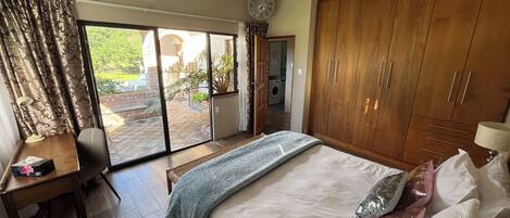 A bedroom with a bed, a desk, a wardrobe, and a sliding glass door leading to an outdoor area.