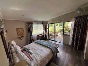 A bedroom with a large bed, a desk, and a view of a garden through a sliding door.