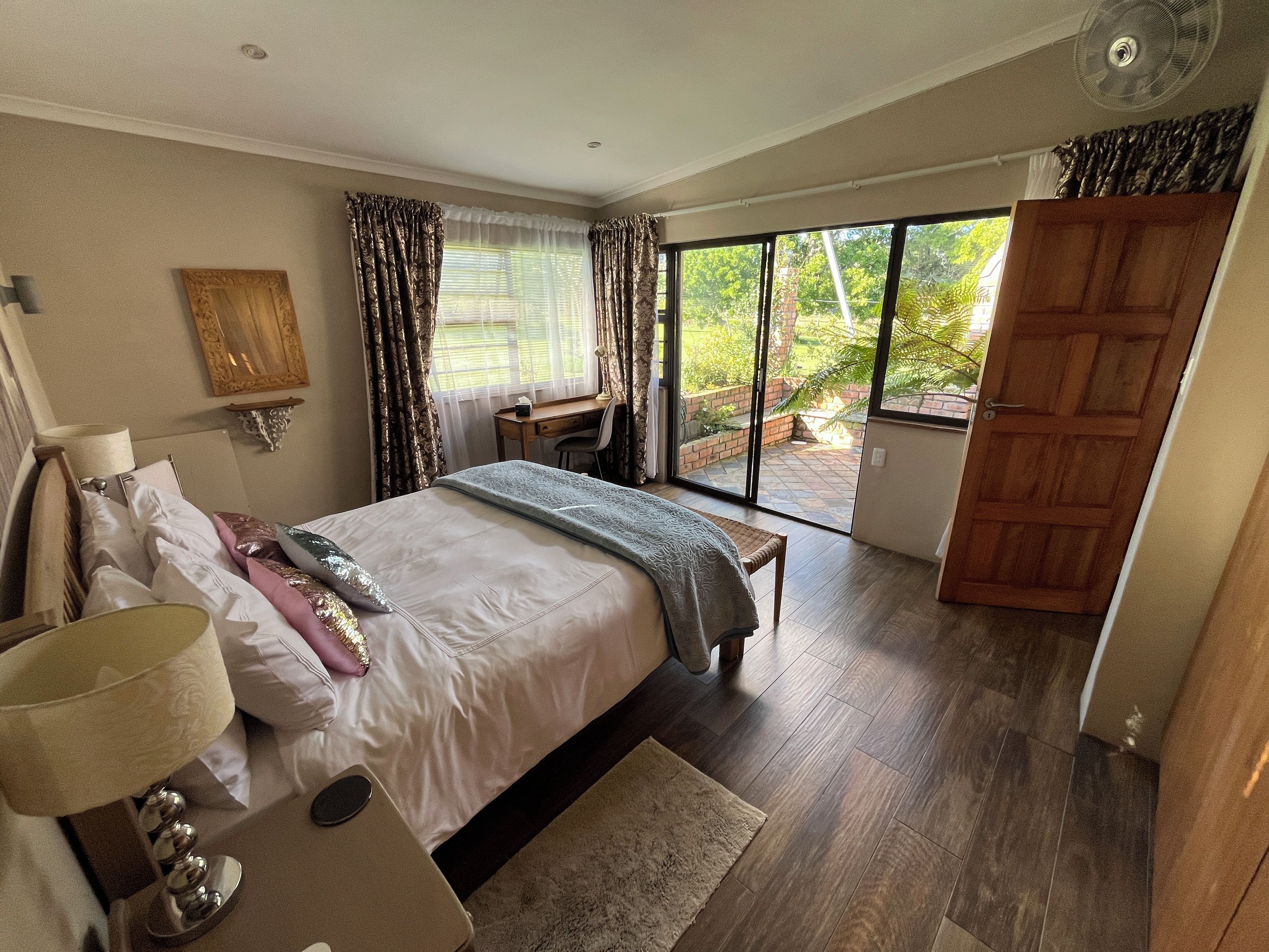 A bedroom with a bed, bedside table, lamp, and a desk with a chair. There is a sliding glass door leading to a balcony.