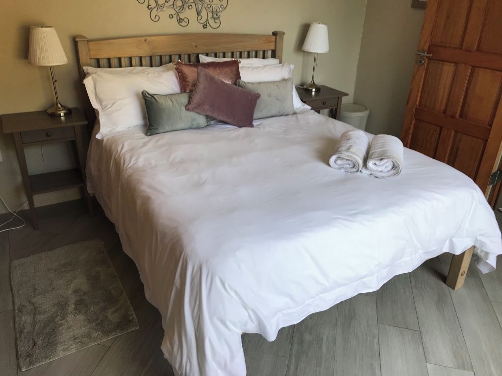 Un lit bien fait, avec du linge de lit blanc et une serviette enroulée, une tête de lit en bois et deux lampes de chevet posées sur des tables de nuit.