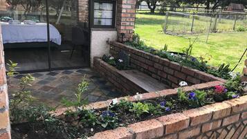 Una stanza con un letto, una finestra e vista su un giardino con un muro in mattoni e piante.