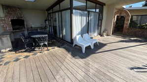 An outdoor patio with a brick fireplace, a table with chairs, and a covered seating area with white plastic chairs. - The Stables (Gqeberha)
