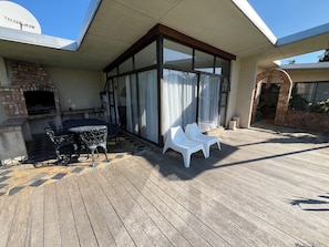 Patio esterno con camino in mattoni, tavolo e sedie, e area salotto coperta con sedie in plastica bianca.