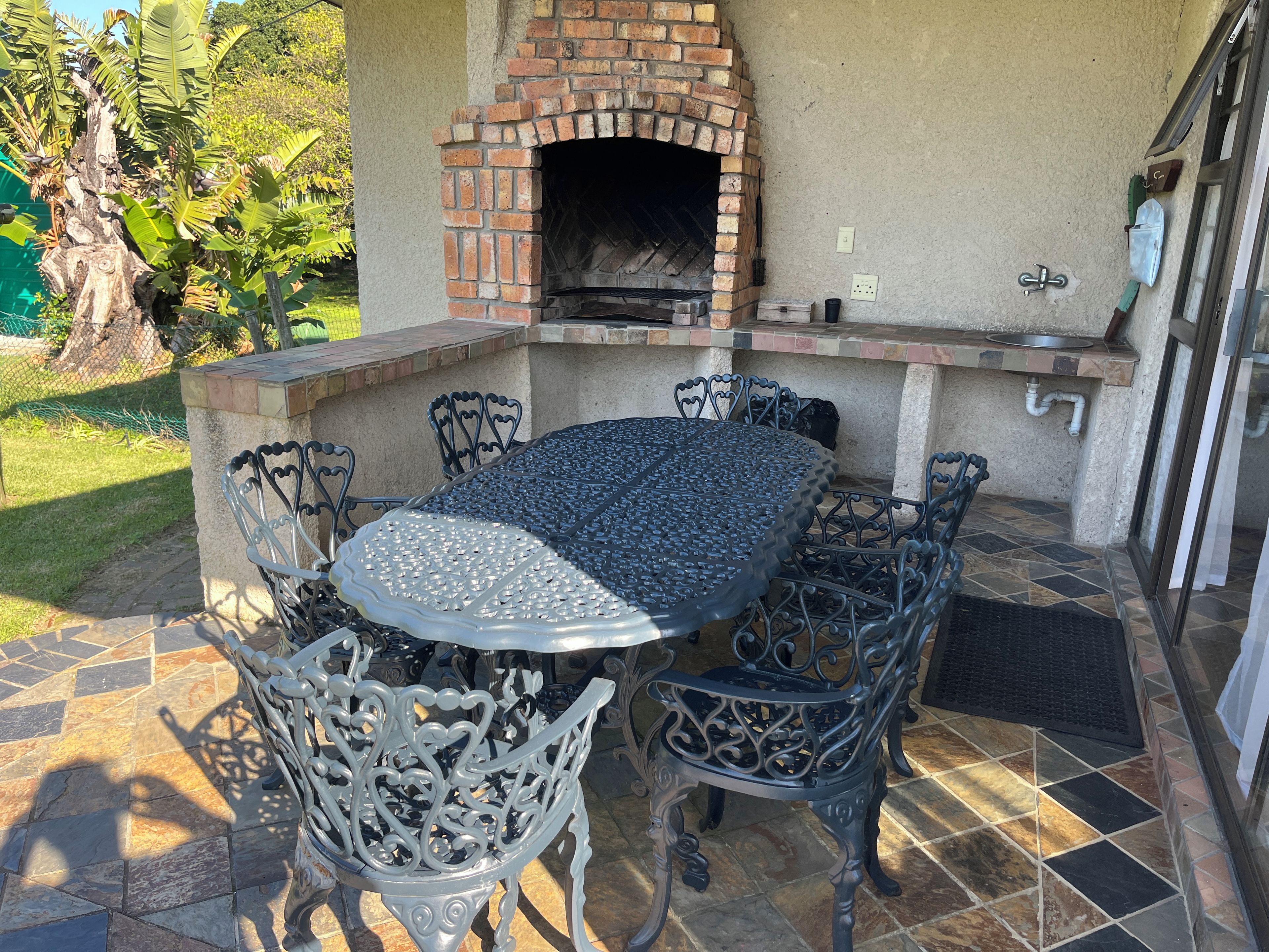 Um pátio ao ar livre com forno de tijolos, uma mesa redonda de metal e cadeiras de metal decoradas.
