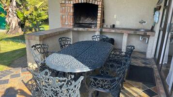 Un patio al aire libre con un horno de ladrillo, una mesa redonda de metal y sillas de metal ornamentadas.