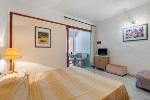 A bedroom with a bed, a desk, a television, and a painting on the wall. - Apartment 'Bilocale Dolores' with Shared Pool, Wi-Fi and Air Conditioning (Campo nell'Elba)