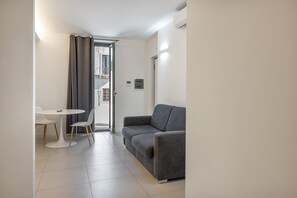 A small, modern living space with a grey sofa, a white table with two chairs, and a door leading to an outdoor area. - Apartment 'Calcagno Home 3' with Private Terrace, Wi-Fi and Air Conditioning (Milazzo)