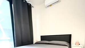 Un dormitori modern amb un llit, una tauleta de nit, un aparell d'aire condicionat i vista cap a l'exterior.