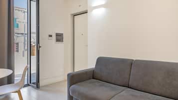 Een modern interieur met een grijze bank, een witte tafel en een glazen deur die leidt naar een buitenruimte.