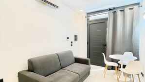Un saló modern amb un sofà gris, una taula rodona petita i dues cadires blanques.