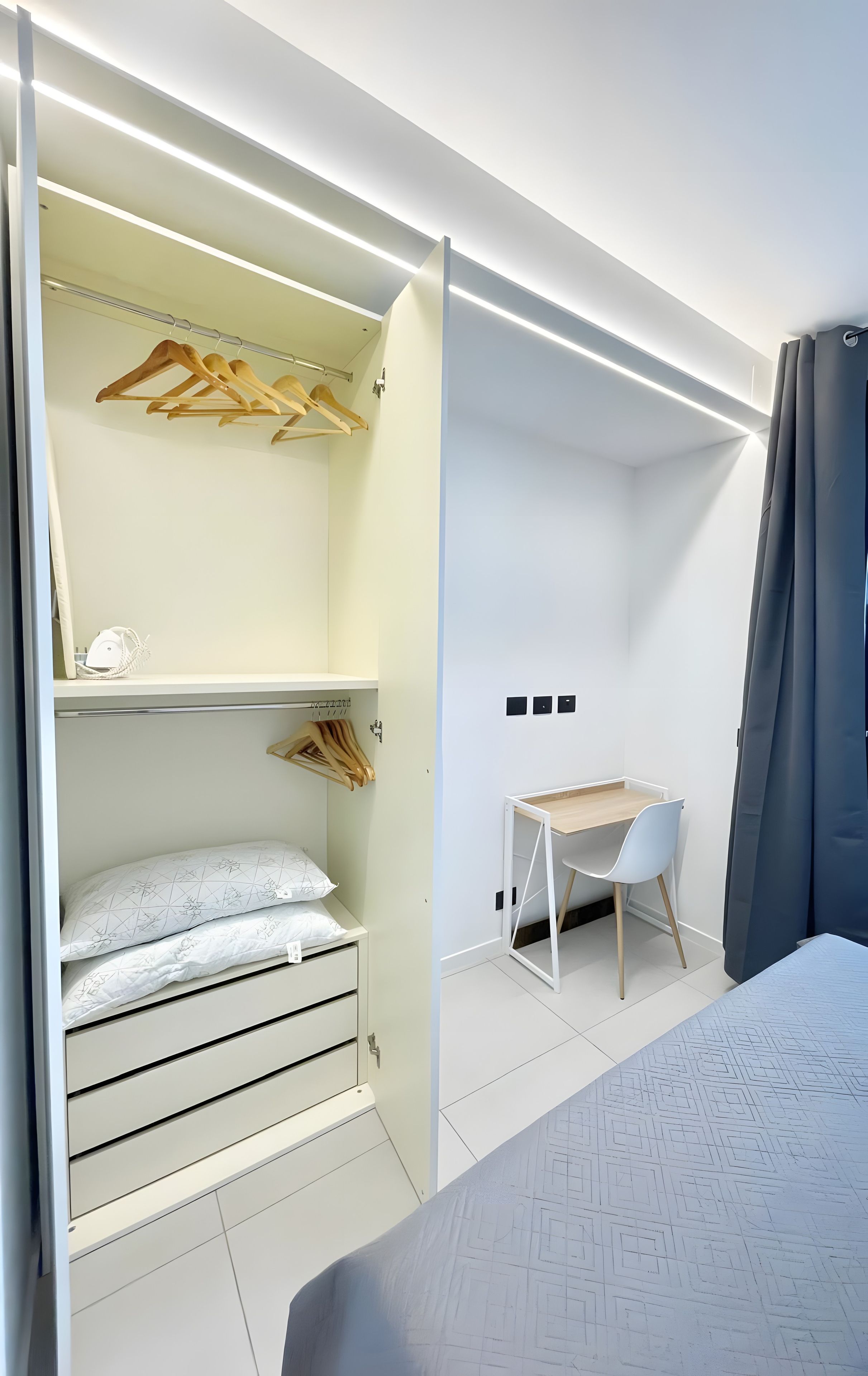 Un dormitorio moderno con cama, escritorio y armario con ropa colgada.