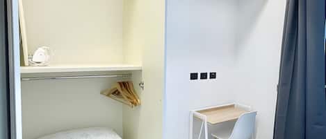 Un dormitorio moderno con cama, escritorio y armario con ropa colgada.