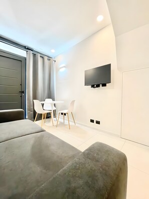 A modern living room with a sofa, two white chairs, a flat-screen TV mounted on the wall, and a sliding door.