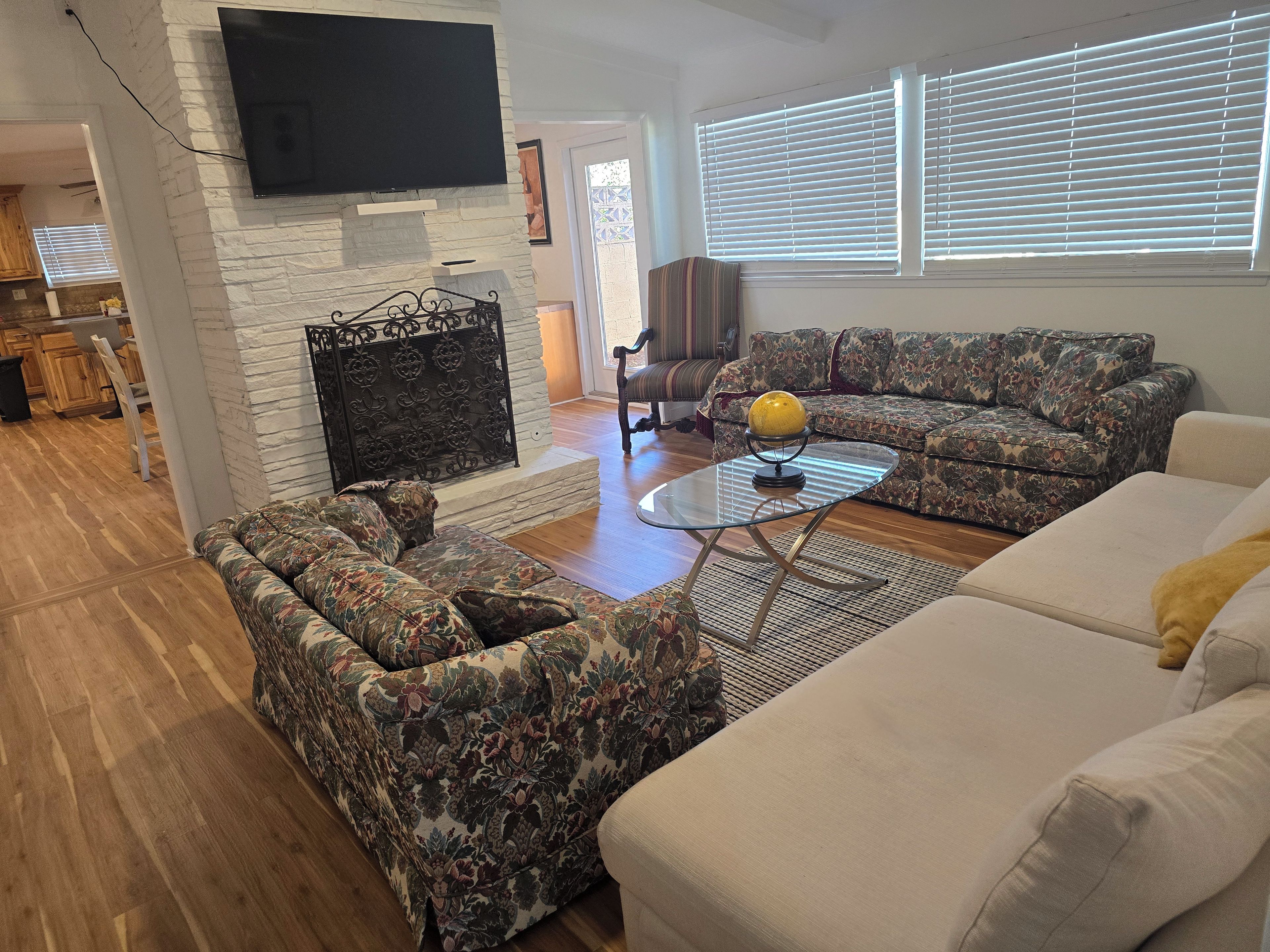 A living room with a flat-screen TV mounted on a stone wall, a patterned sofa, a white sofa, and a coffee table with a globe.