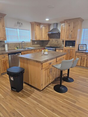 Une cuisine avec des meubles de rangement en bois, un îlot central, un évier, une cuisinière et une poubelle.
