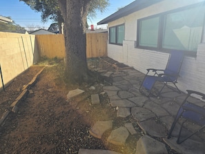 A backyard with a tree, a stone patio, and a blue folding chair. - Amazing 3-bedroom house with AC in enchanting Midland (Midland)