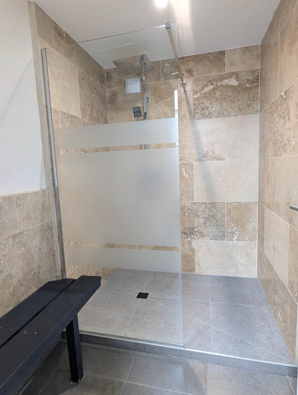 A shower area with a bench, tiled walls, and a glass door.