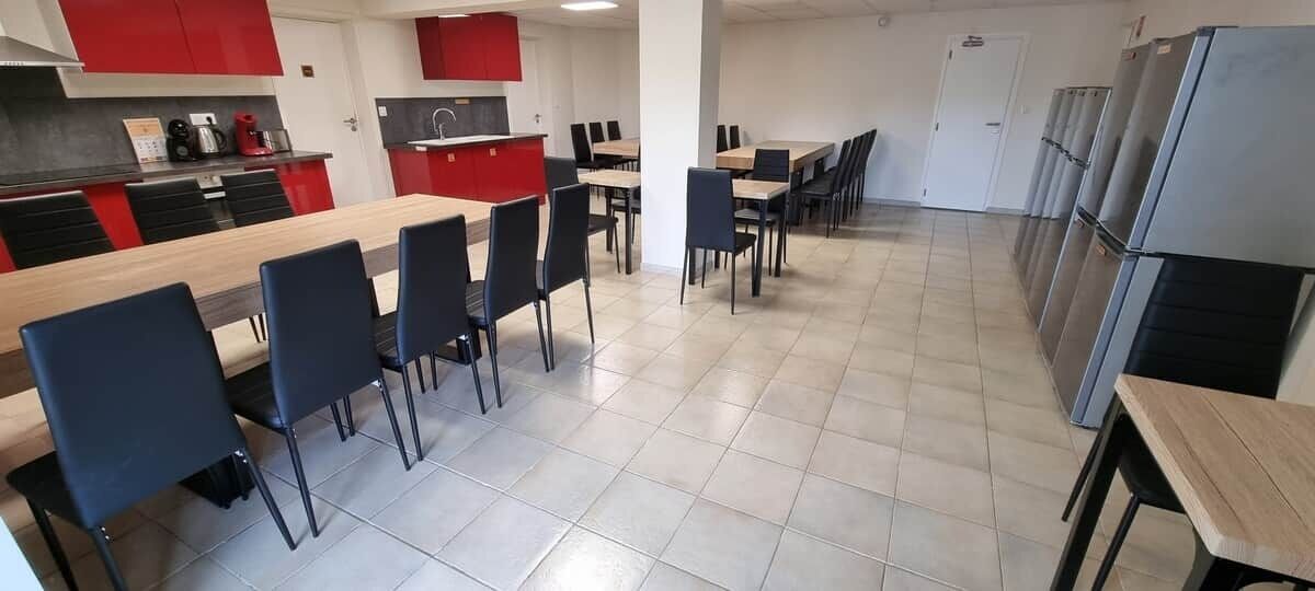 Une cuisine moderne avec des meubles de rangement rouges, une longue table en bois et plusieurs chaises.