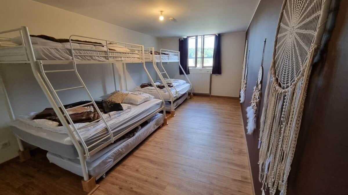 Une chambre de dortoir avec des lits superposés, un radiateur, une fenêtre avec des rideaux et une décoration murale en macramé.