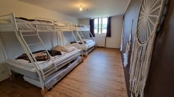 Une chambre de dortoir avec des lits superposés, un radiateur, une fenêtre avec des rideaux et une décoration murale en macramé.