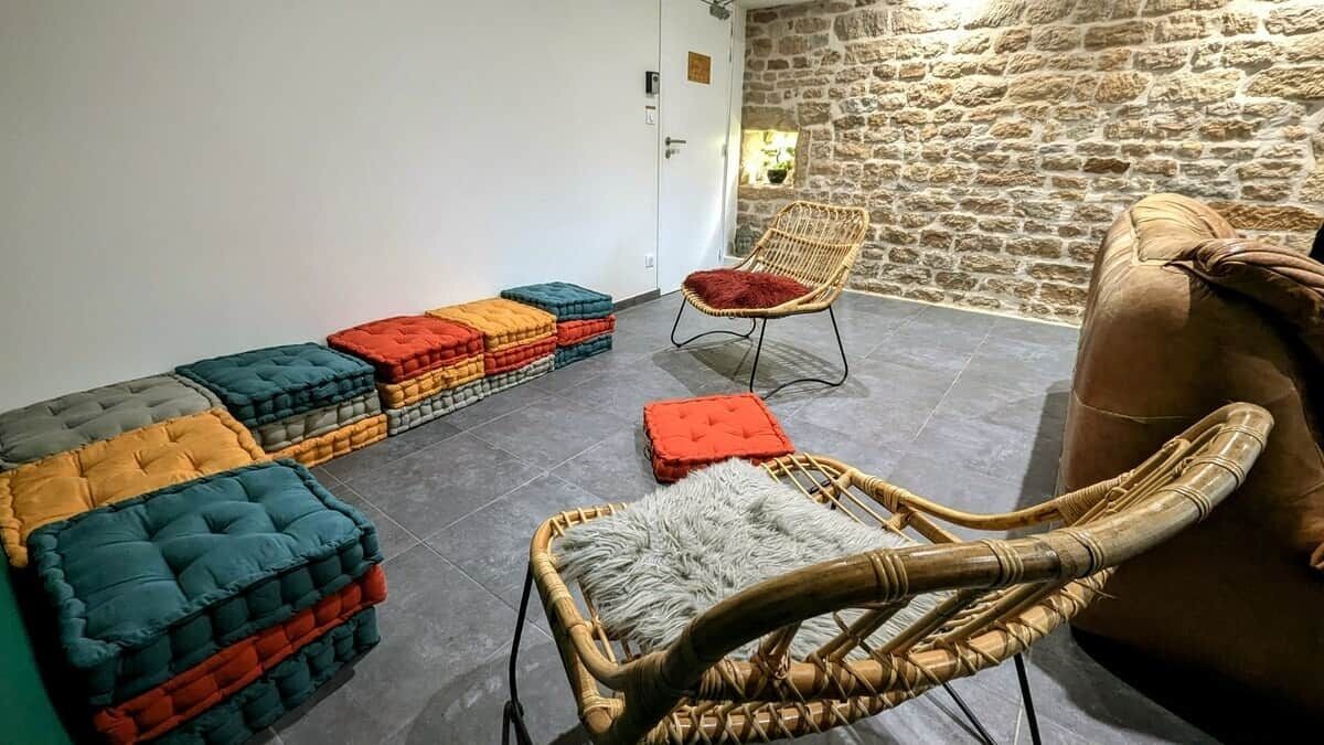 Une pièce avec un mur en pierre, une chaise en osier, un banc rembourré et un canapé.