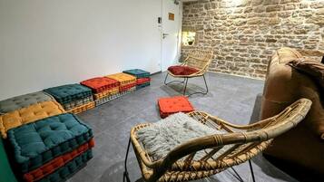 Une pièce avec un mur en pierre, une chaise en osier, un banc rembourré et un canapé.
