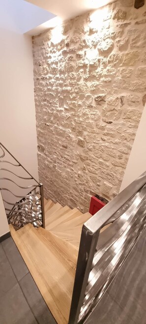A staircase with a textured stone wall, a metal railing, and a wooden floor.