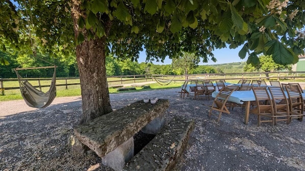 A picnic area with a stone bench, a hammock, and wooden tables and chairs.