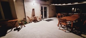 Een terras buiten met een tafel, stoelen, een deur en een wandlamp.