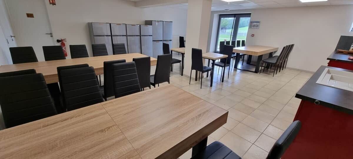Un espace repas avec plusieurs tables et chaises, un coin cuisine équipé d’appareils électroménagers et un comptoir rouge.