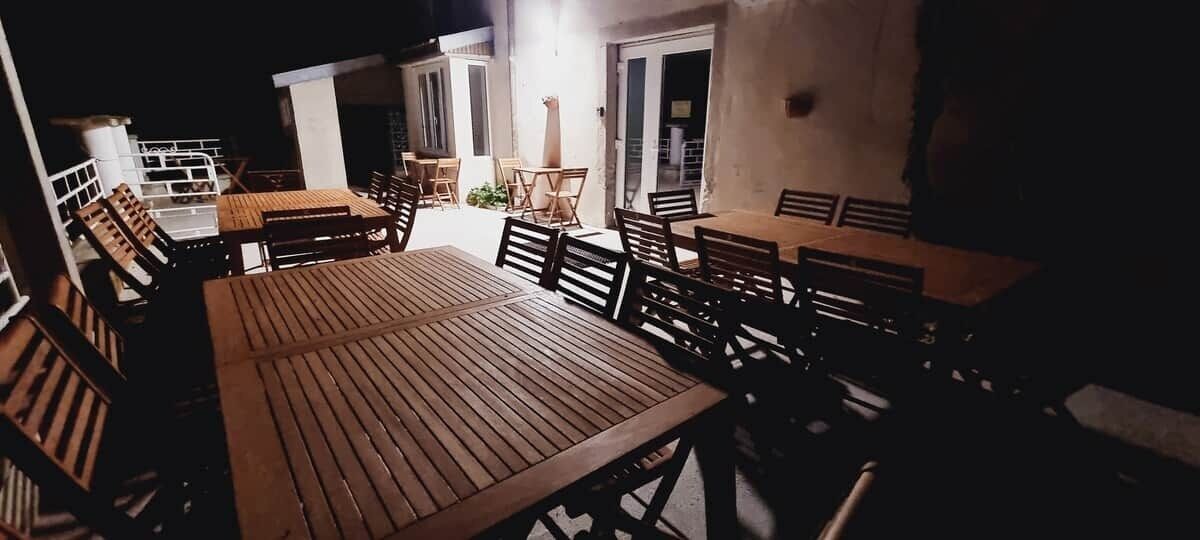 An outdoor patio with wooden tables and chairs, a white wall, and a door.