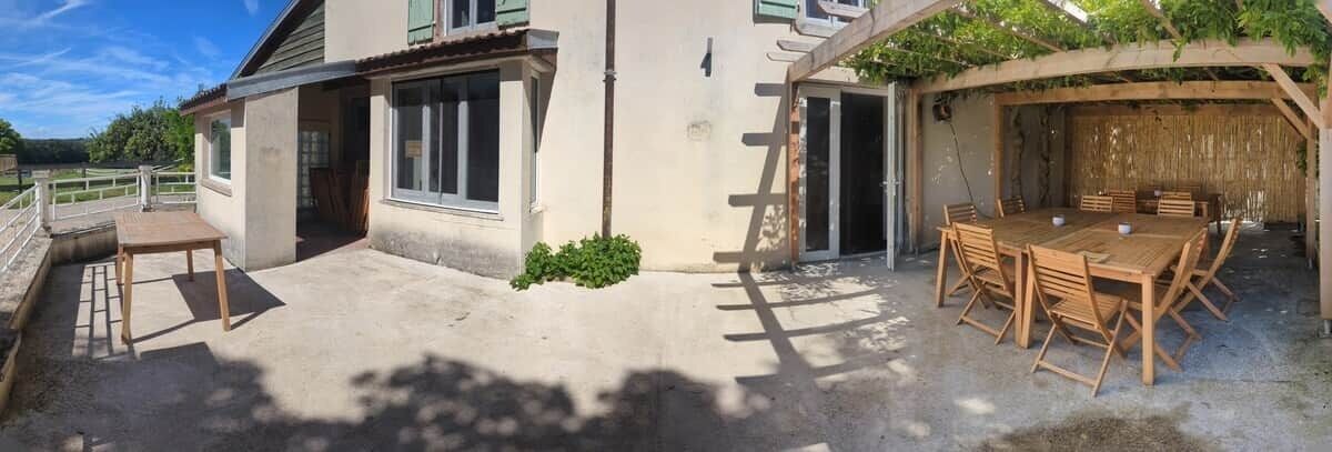 Un espace extérieur abrité, aménagé pour prendre les repas, avec une table et des chaises, une terrasse en béton et un bâtiment doté de fenêtres et d’une porte.