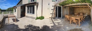 Un espace extérieur abrité, aménagé pour prendre les repas, avec une table et des chaises, une terrasse en béton et un bâtiment doté de fenêtres et d’une porte.