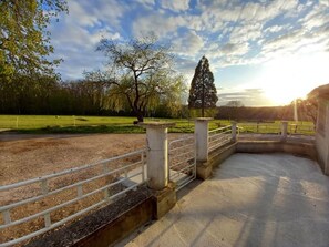 A paved pathway with a metal railing, leading to a grassy area with trees and a clear sky.
