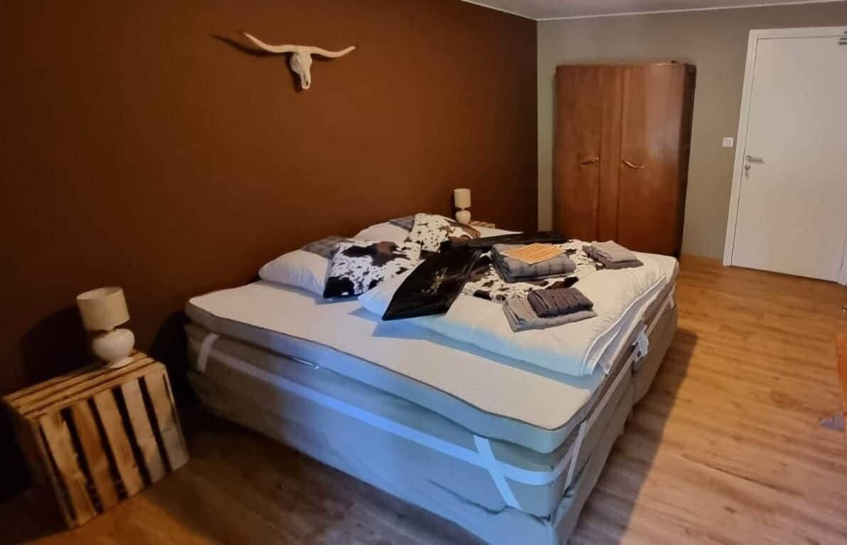 Ett sovrum med en säng, en garderob i trä, en vägglampa och ett nattduksbord i trä.