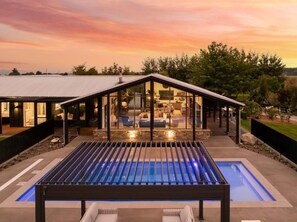 Una casa moderna con un patio de cristal, piscina y jardín cuidado.