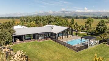Ein modernes Haus mit einer großen Terrasse, einem Swimmingpool und Blick auf Berge.