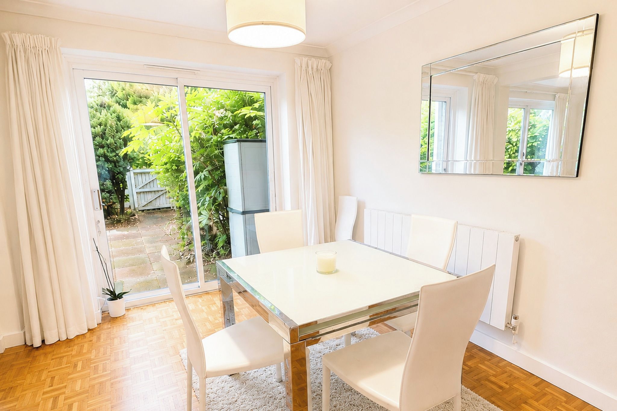 Un coin repas comprenant une table, des chaises, une bougie et une vue sur un jardin, accessible par une porte coulissante.