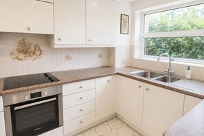 A kitchen with white cabinets, a Bosch oven, a stainless steel sink, and a window with a view of greenery. - Bright 2BDR Flat with King Bed in West London (Greater London)