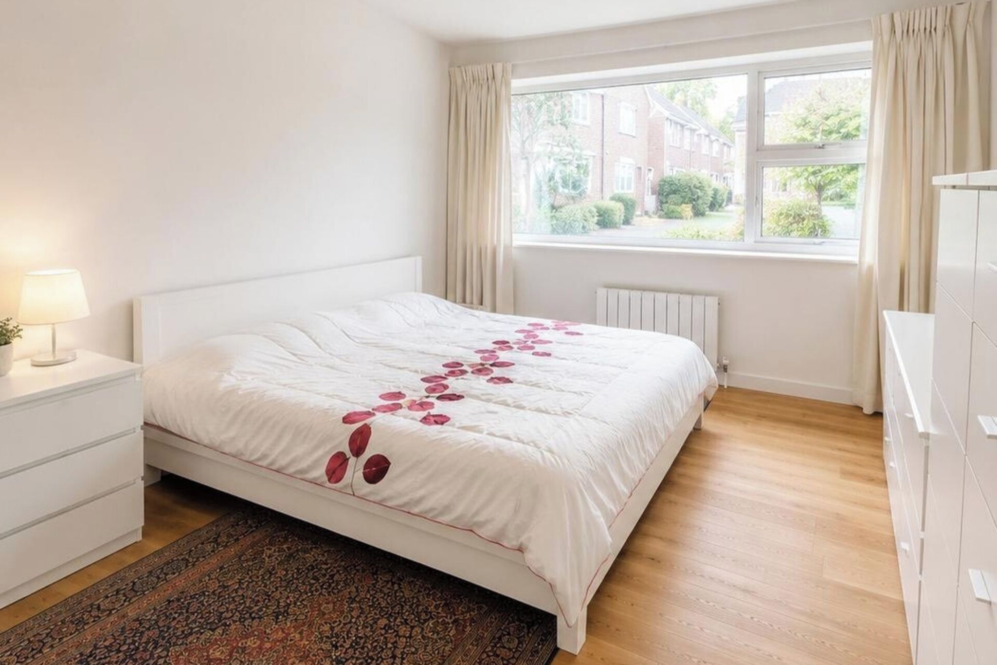 Une chambre à coucher avec un lit, une table de chevet, une fenêtre avec des rideaux et un radiateur.