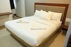 A neatly made bed with white linens and pillows, a wooden headboard, and a small bedside table with a power outlet. - Raghava Residency & Banquet Hall (Hyderabad)