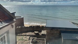 Vista costeira com muro de pedra, pequeno jardim e um edifício com telhado inclinado.